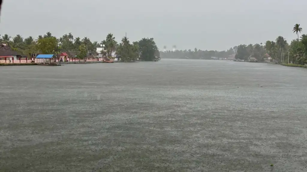 A premium glass-enclosed houseboat cruising smoothly through heavy monsoon rain on lush green Alleppey backwaters in Kerala