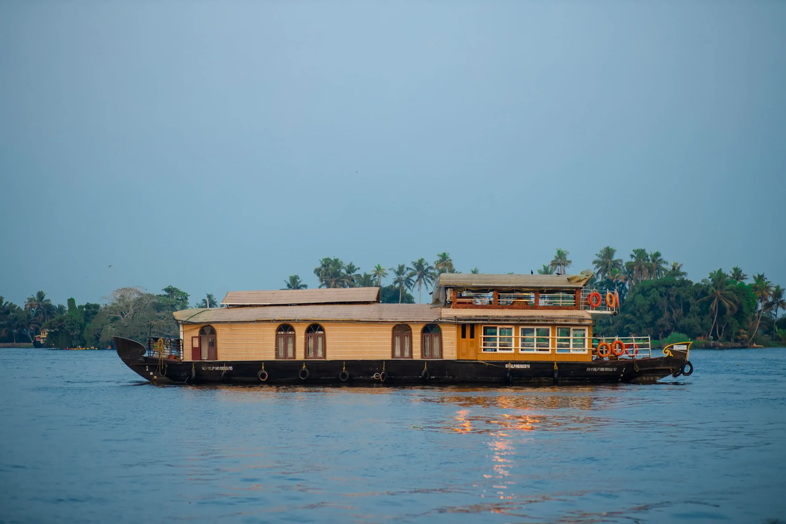 mithtam-mithram02-2-bedroom-premium-houseboat-alleppey Exterior view of Mithtam 2-bedroom premium houseboat with upper deck seating and front glass-covered A/C lounge cruising the Alleppey backwaters